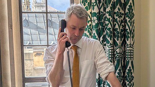 Will Forster Will Forster speaking on the phone in his Westminster office, he is wearing a white shirt with the sleeves rolled up and a yellow tie.