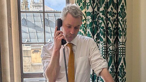 Will Forster Will Forster speaking on the phone in his Westminster office, he is wearing a white shirt with the sleeves rolled up and a yellow tie.