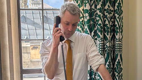 Will Forster Will Forster speaking on the phone in his Westminster office, he is wearing a white shirt with the sleeves rolled up and a yellow tie.
